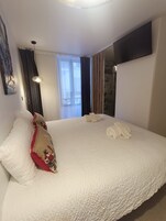 A hotel room with a large bed, a flat-screen TV mounted on the wall, a window with curtains, and a painting on the wall.