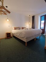 A neatly arranged bedroom with a bed, two bedside tables, a hanging light fixture, and a view of the outside through a window.