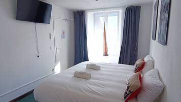 A hotel room with a bed, a flat-screen TV mounted on the wall, a window with curtains, and a ceiling light.