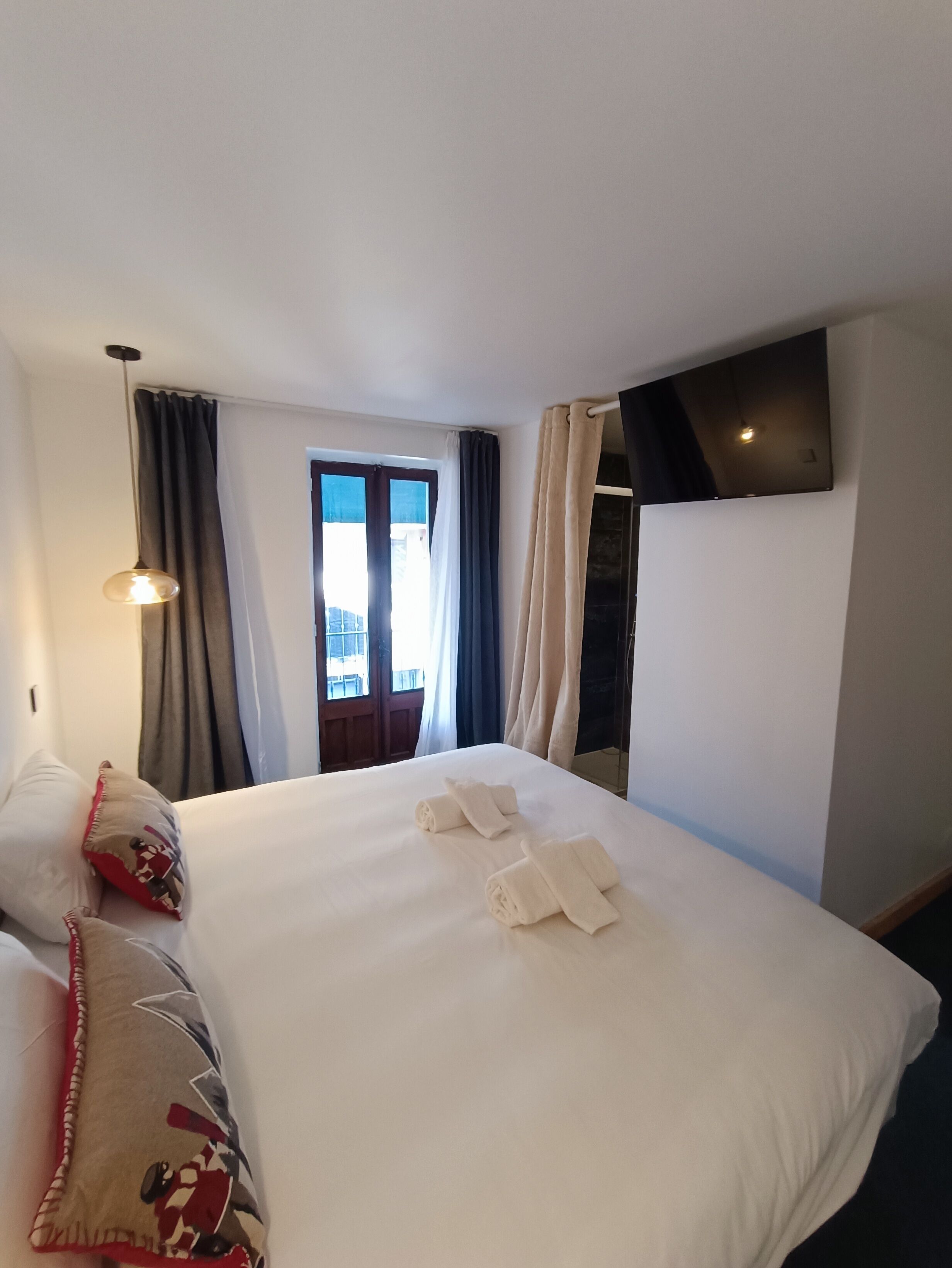 Habitación de hotel con una cama grande, televisión montada en la pared, ventana con cortinas y vistas al exterior.