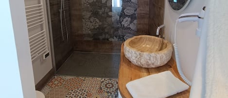 A modern bathroom with a shower, a wooden vanity with a bowl sink, and a large mirror.