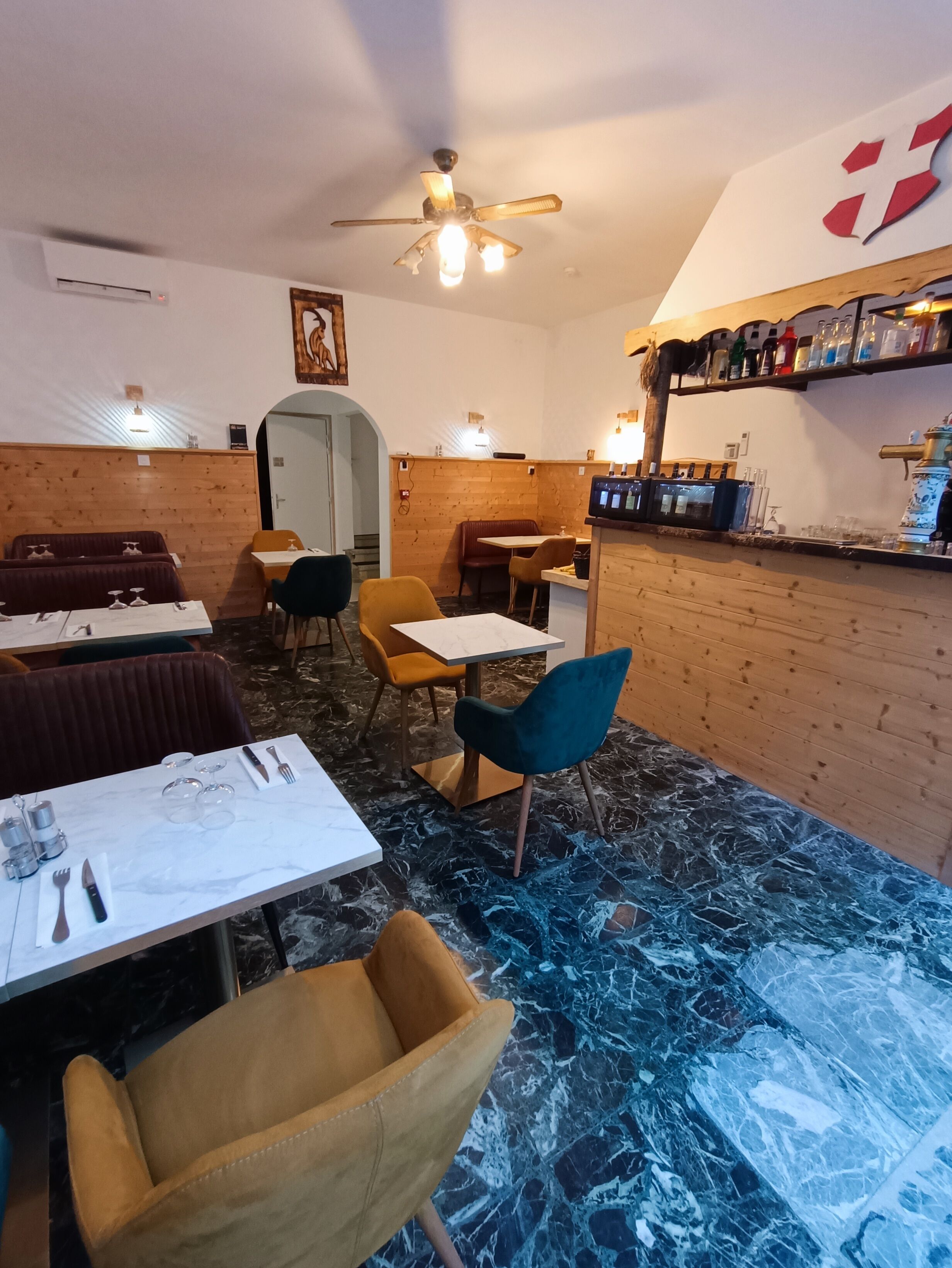 Interior de un restaurante con paredes de madera, pisos de mármol y una zona de bar con botellas.