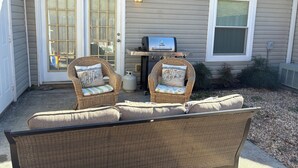 A patio with two wicker chairs, a grill, and a water heater outside a house. - Simple Comfort 2-bedroom home 4.5 miles from the Augusta National Golf Course! (Augusta)