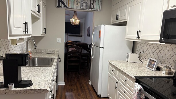 A kitchen with white cabinets, a stainless steel sink, a black coffee maker, a refrigerator, and a microwave. - Simple Comfort 2-bedroom home 4.5 miles from the Augusta National Golf Course! (Augusta)