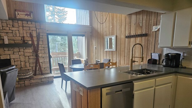 A modern kitchen with a central island, wooden accents, a stone wall, and a dining area with a view. - Recently remodeled first floor, beautiful views of the lifts/mountains! (Mammoth Lakes)