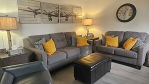 A living room with a grey sofa set, a black leather armchair, a wooden coffee table, and a wall clock. - Recently remodeled first floor, beautiful views of the lifts/mountains! (Mammoth Lakes)