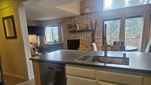 A kitchen with a stone fireplace, a dishwasher, and a dining area with a view of the outdoors. - Recently remodeled first floor, beautiful views of the lifts/mountains! (Mammoth Lakes)