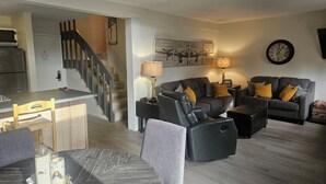 A modern living room with a grey sofa, a dining table, and a staircase leading to another level. - Recently remodeled first floor, beautiful views of the lifts/mountains! (Mammoth Lakes)