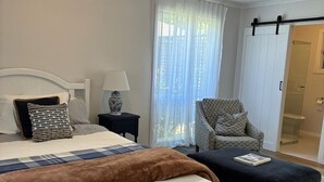 A bedroom with a bed, bedside table, lamp, chair, and a sliding door to a bathroom. - Self-Contained Studio Apartment – Macedon Ranges, Riddells Creek (Riddells Creek)