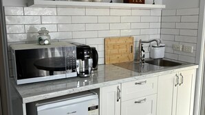 A compact kitchen with white cabinetry, a built-in dishwasher, a coffee maker, and a wooden cutting board. - Self-Contained Studio Apartment – Macedon Ranges, Riddells Creek (Riddells Creek)