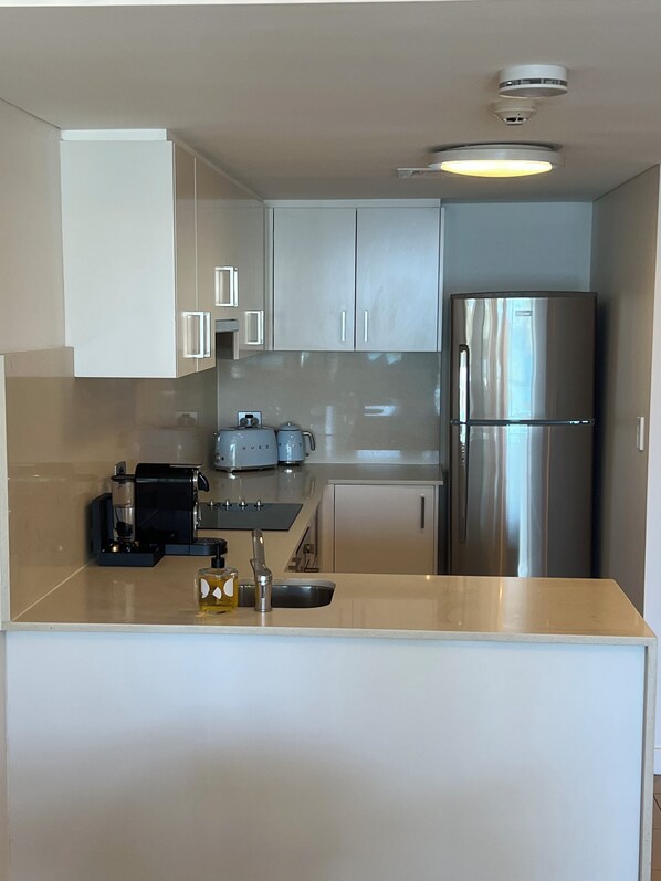 A compact kitchen with a built-in espresso machine, a stainless steel refrigerator, and a light-colored countertop. - Luxe Manly Beachfront Apartment with Harbour Views & Free Parking (Manly)