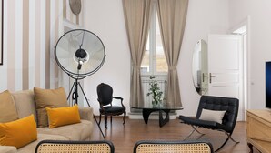 Un salon comprenant un canapé, des fauteuils, une table en verre, un lampadaire, un miroir et une porte.