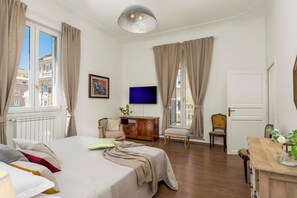 Quarto bem iluminado com cama, televisão e escrivaninha com cadeira.
