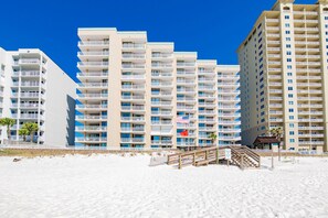 A beachfront hotel with multiple balconies, a sandy beach in front, and a wooden walkway leading to the entrance. - NEW:) 3BR Luxury Oceanfront Bliss! (Orange Beach)
