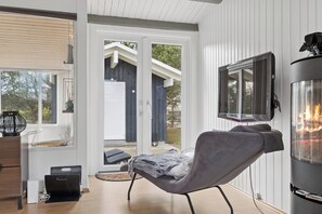 A modern living room with a fireplace, a television, and a sliding glass door leading to an outdoor area. - Lovely holiday home near water and nature (Hadsund)