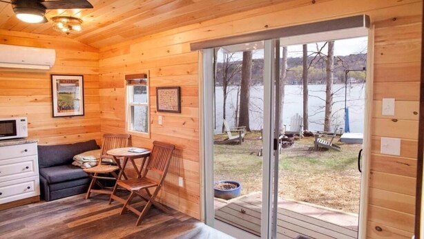 A wooden cabin with a dining area, a sofa, and a view of a lake. - Gorgeous 2-bedroom cottage in charming Hammondsport awaits you (Hammondsport)