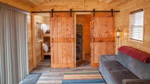 A cozy cabin interior with a wooden floor, a gray sofa, a striped rug, and a sliding door leading to a storage area. - Gorgeous 2-bedroom cottage in charming Hammondsport awaits you (Hammondsport)