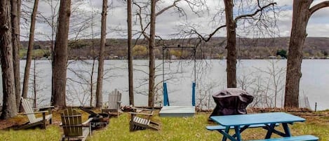 Ein Picknickplatz am Seeufer mit Bänken und einem Tisch, umgeben von Bäumen.