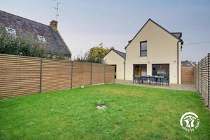 A modern house with a large backyard, a wooden fence, and a dining area with outdoor furniture. - Chez Anne - 4 people (BADEN)