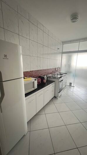 Cozinha moderna com armários brancos, geladeira, micro-ondas, fogão a gás e painel de azulejos.