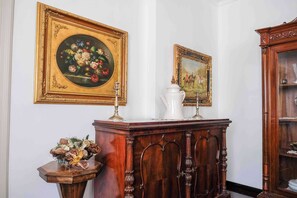 A room with a wooden cabinet, a small table with a floral arrangement, and two framed paintings on the wall. - Luxury Palermo Apartment w/ Hot Tub & City Center Access (Palermo)