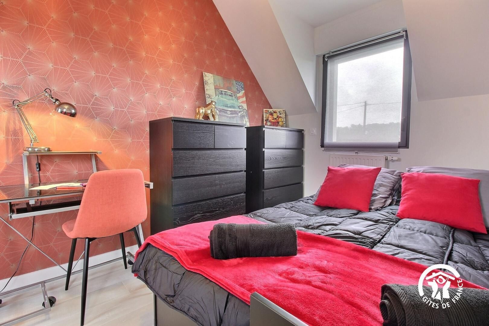 A bedroom with a bed, a desk, a chair, a dresser, and a window.