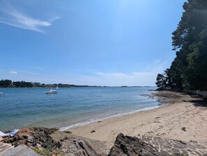 Ein Strand mit klarem, blauem Wasser, sandigem Ufer und Felsen.