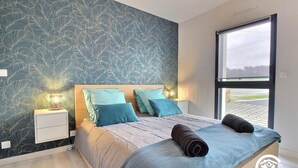 Un dormitorio con una cama grande, una mesita de noche, una lámpara de pared y una ventana con vistas.