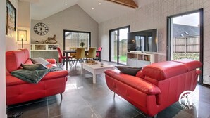 Un salón espacioso con sofás de cuero rojo, un comedor con mesa y sillas, un gran reloj de pared y un televisor.