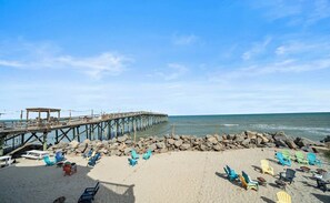 Een strand met een houten pier die zich uitstrekt over de oceaan, omringd door rotsen en kleurrijke strandstoelen.