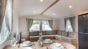 Un espace de repas moderne avec une table en bois dressée pour quatre personnes, un canapé et une vue sur l’extérieur.