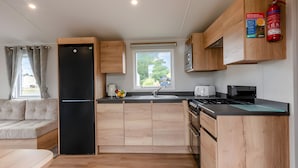 Une cuisine de taille réduite, avec des meubles de rangement en bois, un réfrigérateur noir, un évier et une cuisinière.
