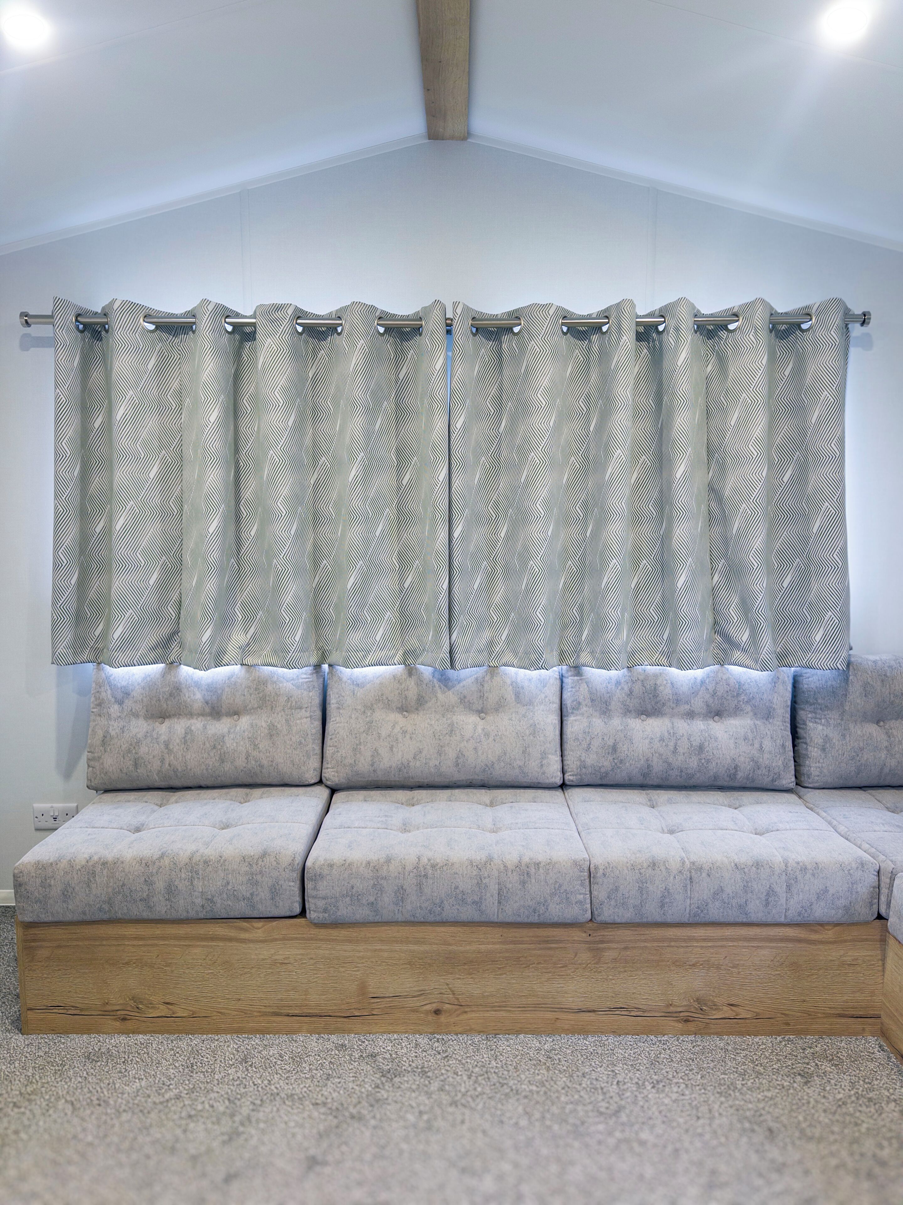 Ein modernes Wohnzimmer mit einem Ecksofa, gemusterten Vorhängen und Holzboden.