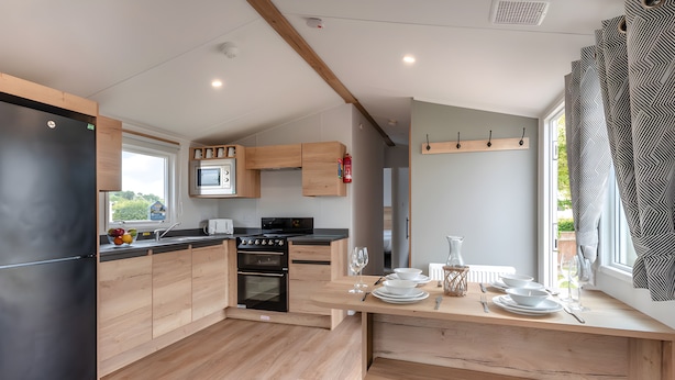 Une cuisine moderne avec des meubles en bois, un four à micro-ondes encastré et un coin repas avec une table mise pour deux personnes.