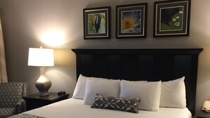 A neatly made bed with a patterned bedspread, a headboard with three framed pictures, a bedside lamp, and a small table with a phone.