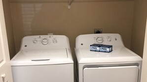 Two stacked front-loading washing machines in a laundry room with a metal shelf above holding folded clothes.