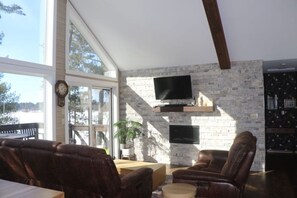 Ein großzügiges Wohnzimmer mit Ledersofas, einem flachbildfernseher, der an einer Steinwand befestigt ist, und einem großen Fenster mit Blick ins Freie.