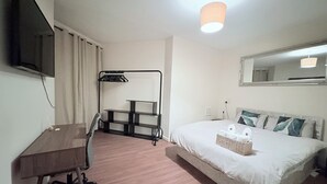 Una camera d'albergo con un letto, una scrivania, una sedia, una TV e una lampada a sospensione.