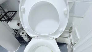 Un water bianco con il coperchio abbassato in un bagno con piastrelle bianche.