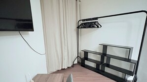 Una stanza piccola con una scrivania in legno, uno scaffale in metallo nero, una TV a muro e una tenda.