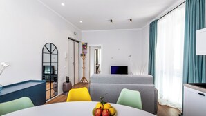 Een moderne woonkamer met een ronde tafel, kleurrijke stoelen, een grijze bank en een televisie.