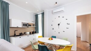 Een moderne keuken met witte kastjes, een magnetron en een spoelbak. Er is een eethoek met een witte tafel en kleurrijke stoelen.
