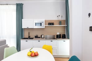 A modern kitchen with white cabinets, a microwave, a sink, and a coffee maker. There is a dining table with a plate of fruit and a yellow chair. - Bright 3 Bed Apartment with 2 Bath near Quirinale (Roma)