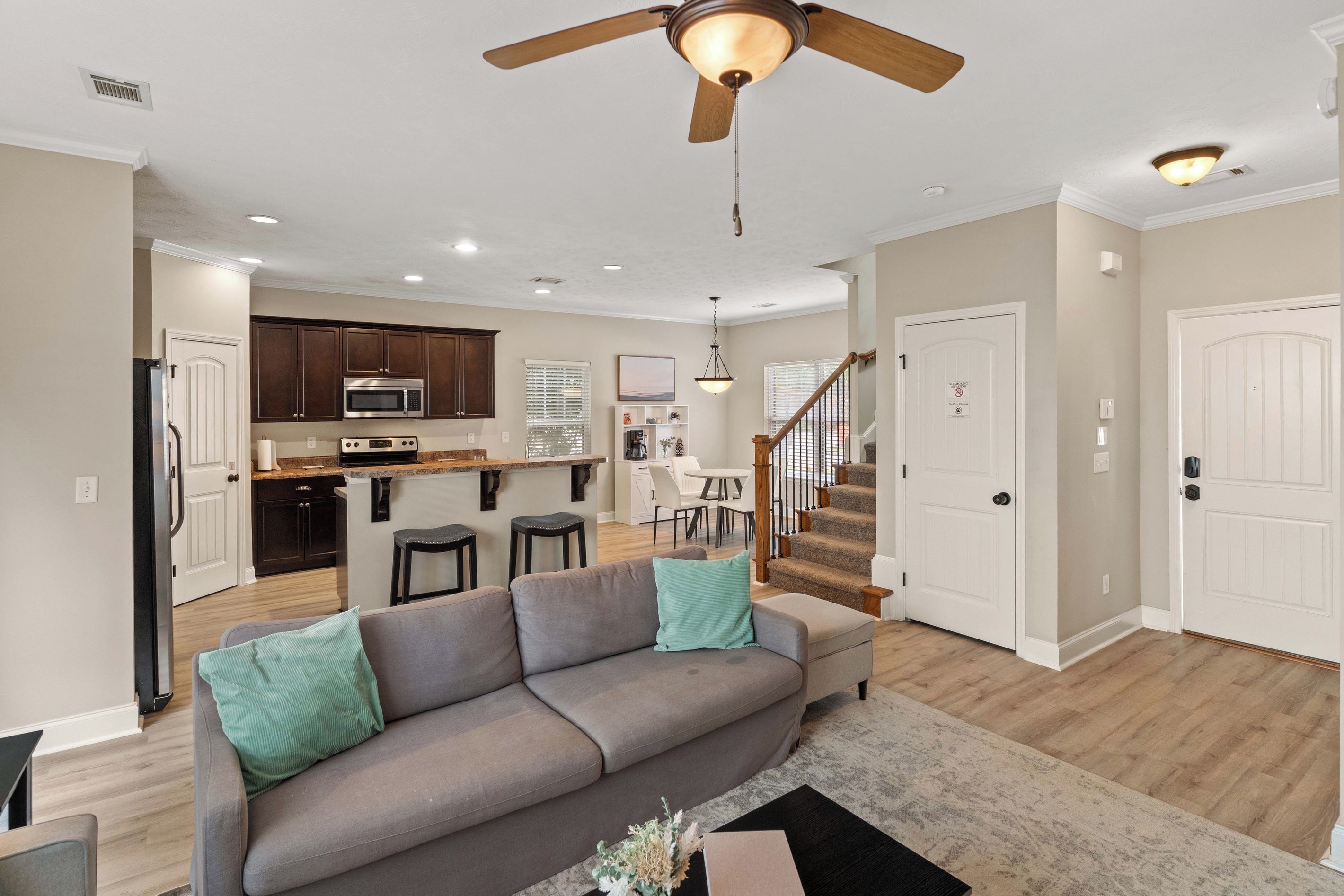 A modern living room with a grey sofa, a ceiling fan, and a kitchen in the background.