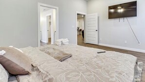 Een slaapkamer met een groot bed, een flatscreen televisie aan de muur en een deur naar een andere kamer.