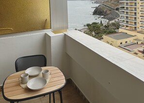 Een balkon met een tafel voor twee personen, met uitzicht op de kust, een gebouw en palmbomen.