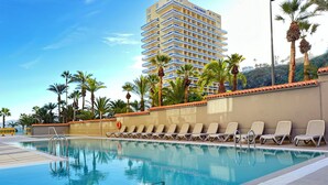 A swimming pool with lounge chairs and palm trees, surrounded by a building with balconies. - Palmeraie Studio - Sea view and pool (Puerto de la Cruz)