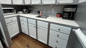 A compact kitchen with white cabinets, a microwave, a coffee maker, and a sink.