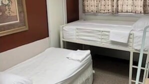 A room with two single beds, a framed picture on the wall, a window with patterned curtains, and a door.