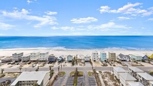 Un hotel frente al mar con vista a la playa, que cuenta con una hilera de edificios y estacionamiento al frente.